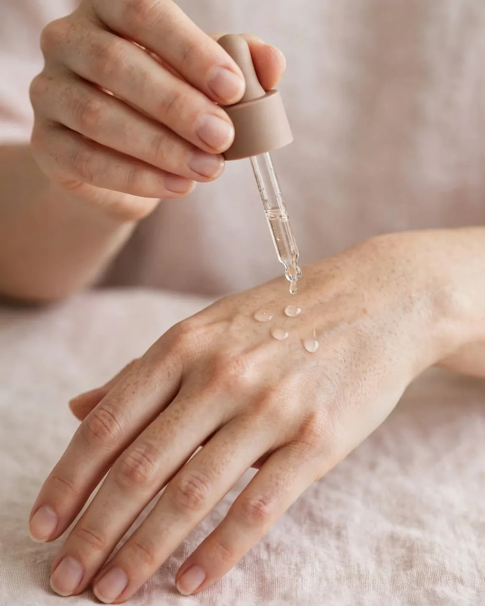 Manos aplicando gotas de sérum sobre el dorso de la mano